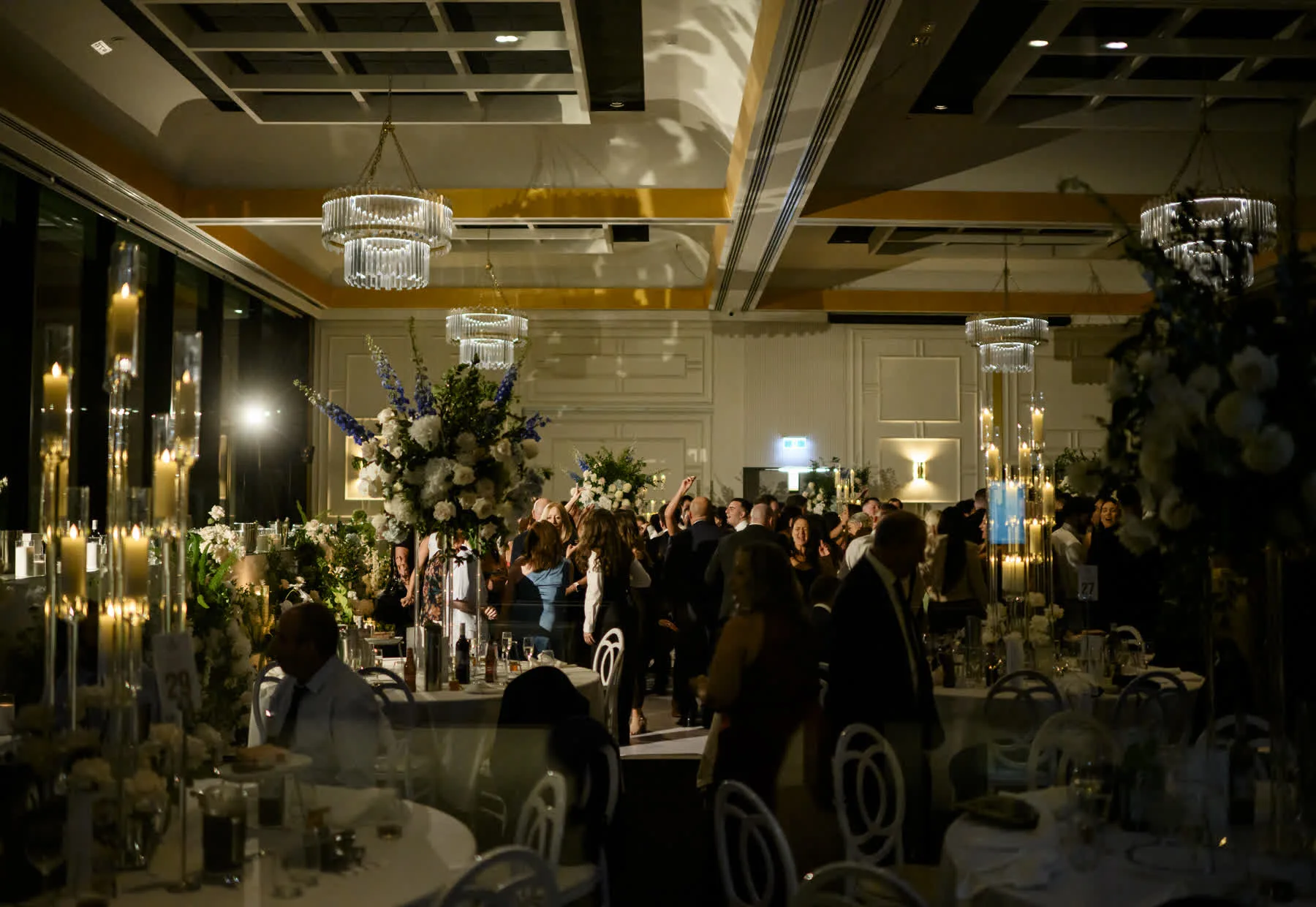 Ballroom wedding reception in Sydney with guests on the dance floor beneath crystal chandeliers and tall white floral arrangements